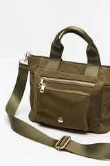 Cartera de mano color verde militar, confeccionada en nylon. Cuenta con doble asa corta, correa larga regulable y desmontable, cierre superior y múltiples bolsillos externos con cierre dorado.