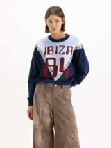 Buzo azul marino y celeste con diseño en bloques, detalles de encaje blanco y estampado frontal con el texto "IBIZA 84" en tono bordó.