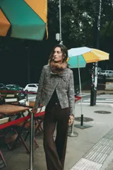 Chaqueta de tweed en tonos gris y negro, con cuello desmontable de pelo sintético marrón, bolsillos delanteros de plastrón y acabados deshilachados.