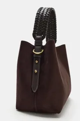 Bolso de mano de formato saca, confeccionado en material tipo gamuza color marrón oscuro, con asa superior trenzada en color negro.