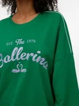 Buzo blanco oversize de manga larga con cuello redondo, ribetes en contraste en las mangas y estampa frontal con la inscripción "BALLERINA EST. The 1976".