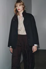 Chaqueta negra de la colección Zara Woman, confeccionada en hilatura con mezcla de algodón. Presenta un cuello alto brillante en contraste de color marrón oscuro, manga larga, bolsillos delanteros y pespuntes marcados. El forro interior es a contraste y el cierre frontal es con botones.