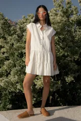 Vestido corto tipo camisero confeccionado en algodón a rayas finas en tonos neutros, de silueta amplia y falda con volados. Diseño abotonado y cuello clásico.