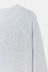 Jersey de punto color gris claro con hilo metalizado, de cuello redondo y manga larga. Bajo recto con aberturas laterales.