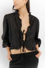 Blusa negra de lino con acabado brillante, de manga larga abullonada, escote con volados y cierre frontal con tiras para anudar.