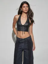 Top halter de cuero sintético negro con escote en V profundo, detalles de ojales metálicos y cordón ajustable frontal.