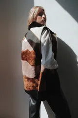 Chaleco largo de piel de oveja con bloques de color en tonos marrón, beige y blanco. Tiene cuello solapa y cierre con un botón forrado en piel.