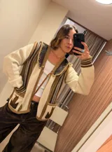 Cardigan tejido de punto en tonos crudo, beige y marrón, con detalles de cuero en el cuello y bolsillos frontales. Presenta diseño rayado, mangas largas y cierre con botones y lazo.