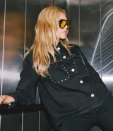 Campera overshirt de denim negro con cuello camisero, bolsillos frontales con solapa, mangas largas y aplicación de tachas metálicas en el pecho y los hombros.