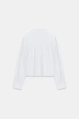 Camisa de popelín color verde militar, con cuello solapa, mangas largas abullonadas terminadas en puño, bajo recto y cierre frontal con botones ocultos por solapa.