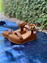 Sandalias de plataforma con tiras de cuero metalizado color dorado y base de plataforma color marrón. Cierre con hebilla ajustable en el tobillo.