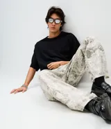 Pantalón de sarga de algodón con corte super baggy, tiro bajo y piernas ultra amplias. Presenta un estampado integral con efecto marmorizado o dirty, bolsillos utilitarios laterales, bolsillos frontales y traseros, cintura con pasantes y cierre frontal con botón y cremallera.