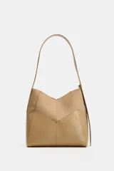 Bolso de hombro color tostado con diseño estructurado que combina paneles de cuero liso y gamuza con pespuntes visibles. Cuenta con un asa larga de hombro ajustable y cierre superior con botón imantado.