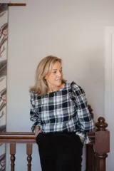 Blusa de manga larga con estampado de cuadros en tonos blanco, negro y gris. Presenta un diseño con volados en los hombros y mangas amplias con puños, confeccionada en una mezcla de poliéster y lana.