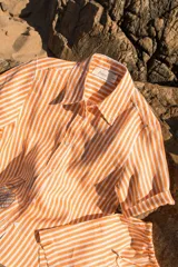 Camisa de manga corta oversize en lino rayado, con cuello camisero, cierre frontal con botones y bordado playero en el frente.
