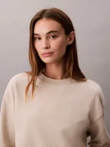 Buzo de felpa Calvin Klein de color beige, con cuello redondo, manga larga y detalles de canalé en cuello, puños y bajo. Presenta un emblema con logo texturizado en el pecho.