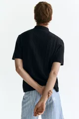 Camisa en punto trenzado de mezcla de algodón, modelo de manga corta con cuello, cierre frontal de botones y bajo recto con remate acanalado.