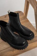 Botas tipo chelsea de cuero negro con textura granulada, paneles laterales elásticos y suela track robusta de goma.