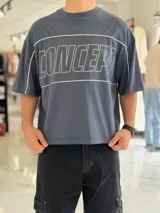 Remera gris oscuro con corte boxy fit de manga corta y cuello redondo. Cuenta con un diseño gráfico frontal con la palabra "CONCEPT" en grandes letras blancas delineadas y líneas decorativas horizontales y en las sisas.