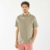 Camisa de manga corta color verde oliva con cuello clásico y cierre abotonado. Presenta un sutil estampado floral bordado en toda la prenda.