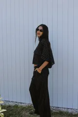 Pantalón negro de pierna ancha con rayas verticales finas, bolsillos laterales, cierre frontal con botón y cordón ajustable en la cintura.