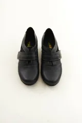 Zapato de cuero negro con cierre de velcro ancho y costuras pespunteadas a contratono.