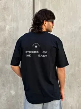Remera negra de corte oversize con estampado en la espalda que dice 'REAL ADVENTURE STORIES OF THE EAST'.