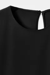 Vestido corto negro sin mangas con hombreras, cuello redondo y bajo asimétrico con una caída lateral más larga. Cuenta con cierre en la espalda con abertura y botón.