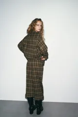 Pantalón bombacho de tiro medio con estampado a cuadros en tonos verde militar, negro y blanco. Presenta bolsillos laterales ocultos, cierre frontal con cremallera y botón, y bajo abullonado con puño y botón.