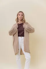 Cardigan tejido liviano color beige con efecto brillante y calados en las mangas. Diseño abierto y corte relajado.