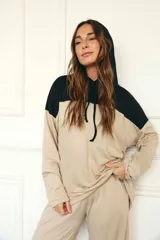 Sudadera con capucha de manga larga, color beige, con canesú negro en la parte superior de los hombros y capucha negra. Presenta cordones negros para ajustar la capucha.