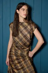 Conjunto de dos piezas compuesto por una blusa de cuello redondo y mangas cortas con ajustes laterales y una falda midi de corte evasé con cintura elástica. Ambas prendas están confeccionadas en tela con estampado de cuadros escoceses y detalles en hilo dorado.