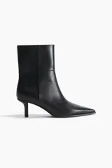 Botines de caña media con punta fina y taco fino tipo kitten heel. Presentan un diseño minimalista con costuras laterales visibles y cierre lateral.