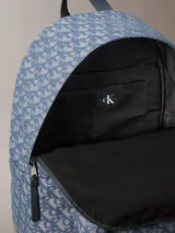Mochila de poliéster reciclado con estampado de logo jacquard en tonos azul y gris. Presenta asa de mano superior, correas acolchadas ajustables, cierre de cremallera y bolsillo frontal con cremallera.