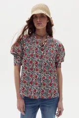 Camisa blanca de algodón con cuello mao, botonera oculta, mangas cortas estilo raglán con cortes estructurados y un bolsillo frontal con cierre.