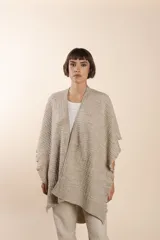 Ruana color crema tejida en punto fantasía con efecto de volado en los bordes.