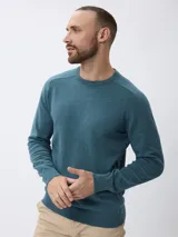 Sweater de tejido de punto fino en color gris, con cuello redondo, mangas largas y puños acanalados. Presenta un diseño liso con un pequeño detalle bordado en el pecho.