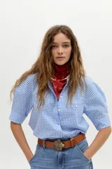 Camisa blanca de algodón con cuello mao, botonera oculta, mangas cortas estilo raglán con cortes estructurados y un bolsillo frontal con cierre.