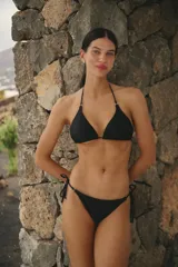 Conjunto de bikini color negro confeccionado en lycra mate. El corpiño es de estilo triangular con breteles ajustables y detalles metálicos. La bombacha es de corte vedetina con laterales ajustables mediante tiras y detalles metálicos en los extremos.