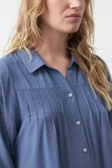 Camisa de manga larga en color celeste, con diseño de corte relajado, cuello clásico y detalle de tablas verticales en el frente.
