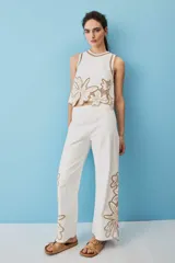 Pantalón blanco de corte recto y tiro alto, con detalles de bordados florales calados en los laterales de las pantorrillas.