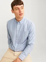 Camisa de vestir de manga larga con cuello abotonado y bolsillo frontal. Presenta un diseño de rayas verticales en tonos azul y blanco, con cierre frontal de botones.
