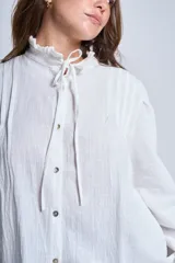 Camisa de color azul con cuello alto decorado con volados y lazo de ajuste. Presenta tablas decorativas en los hombros, cierre frontal con botones de nácar y mangas largas con puños elásticos que generan un efecto abullonado.