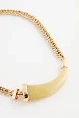 Collar dorado con cadena de eslabones gruesos y un dije central en forma de cuerno curvo de resina color verde claro.