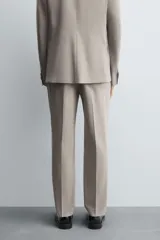 Pantalón de vestir slim fit en color beige, confeccionado en tejido con lana. Presenta cierre frontal con cremallera y botón, bolsillos laterales y bolsillos traseros de doble vivo con botón.