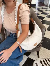 Cartera tipo hobo de cuero color crudo con correa de cuero marrón.