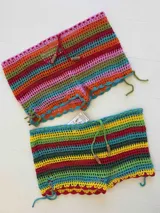 Short tejido a crochet con diseño de rayas horizontales multicolores. Presenta cintura ajustable con cordón y cuentas decorativas de madera, además de un borde inferior con terminación festoneada.