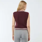 Chaleco de tejido de punto color bordó, sin mangas, con cuello redondo y puños acanalados con doble franja blanca. Presenta un patrón de trenzas verticales.