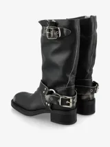 Bota de caña media de cuero negro, estilo biker, con caña arrugada y detalles de correas con hebillas metálicas plateadas en la parte superior y alrededor del tobillo. Posee un taco bajo y grueso.