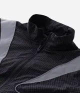 Campera liviana de poliamida con diseño cuadrillé sutil, cuello alto y cierre frontal. Presenta paneles reflectivos estratégicos para mayor visibilidad, puños elásticos y corte contemporáneo.